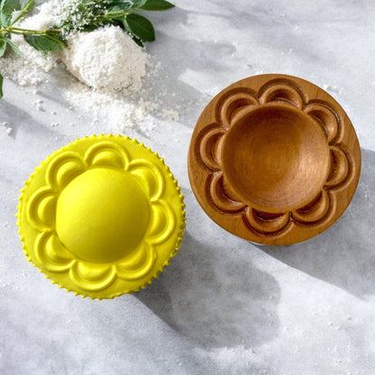 Yellow silicone mold and wooden mold on a textured surface with greenery.